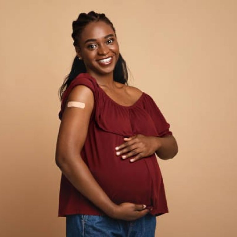 Safety vaccination during pregnancy cocnept. Cheerful pregnant young black woman got vaccinated against COVID-19, showing her arm with band on and hugging her big tummy, expecting baby, copy space