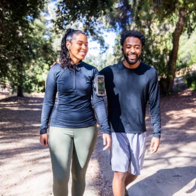 A black man and Latina woman walking on a trail after a workout