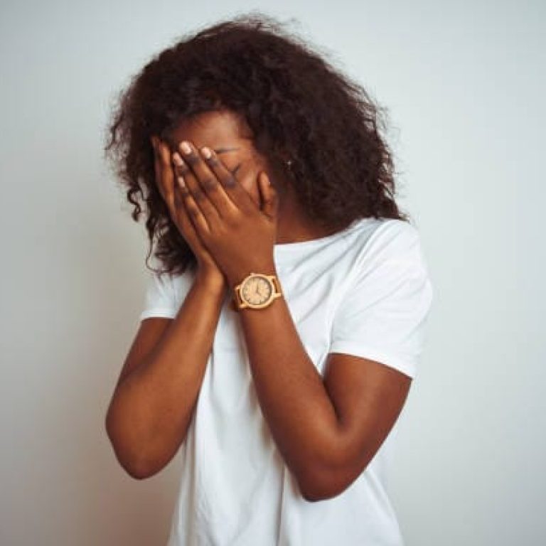 Young african american woman wearing t-shirt standing over isolated white background with sad expression covering face with hands while crying. Depression concept.