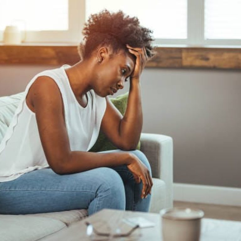 Side view young woman looking away at window sitting on couch at home. Frustrated confused female feels unhappy problem in personal life quarrel break up with boyfriend or unexpected pregnancy concept