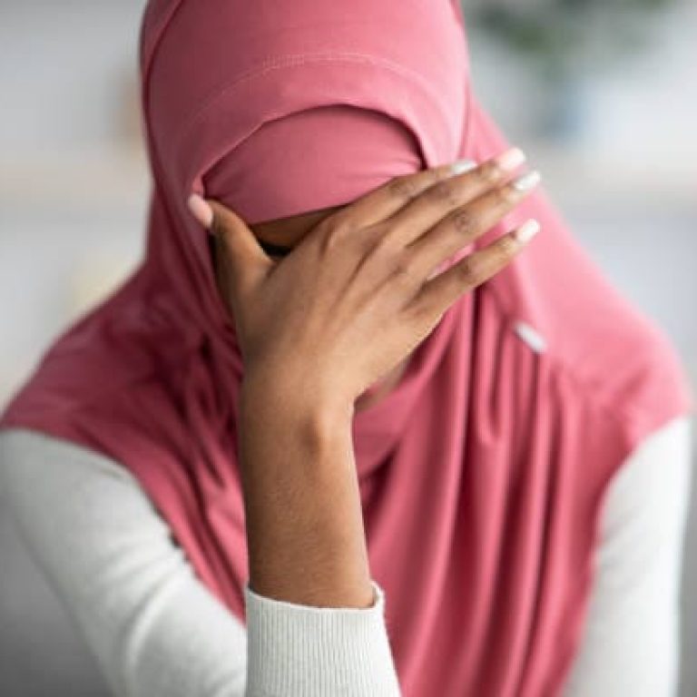 Portrait Of Desperate Black Muslim Woman In Hijab Sitting At Home, Depressed African Islamic Female In Headscarf Covering Eyes With Hand, Suffering From Domestic Violence Or Nervous Breakdown