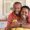 Happy mature black couple bonding to each other and smiling while sitting on couch. Portrait of smiling black man embrace his wife from behind and looking at camera. Smiling husband and beautiful woman laughing.