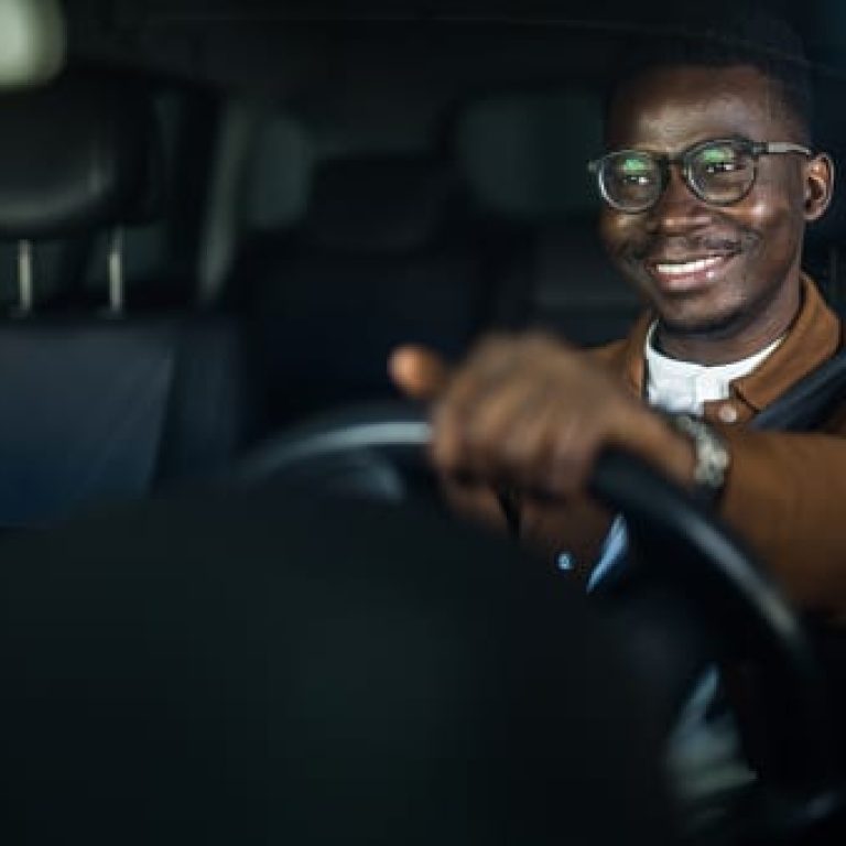 Cheerful young African American man enjoys driving his car.