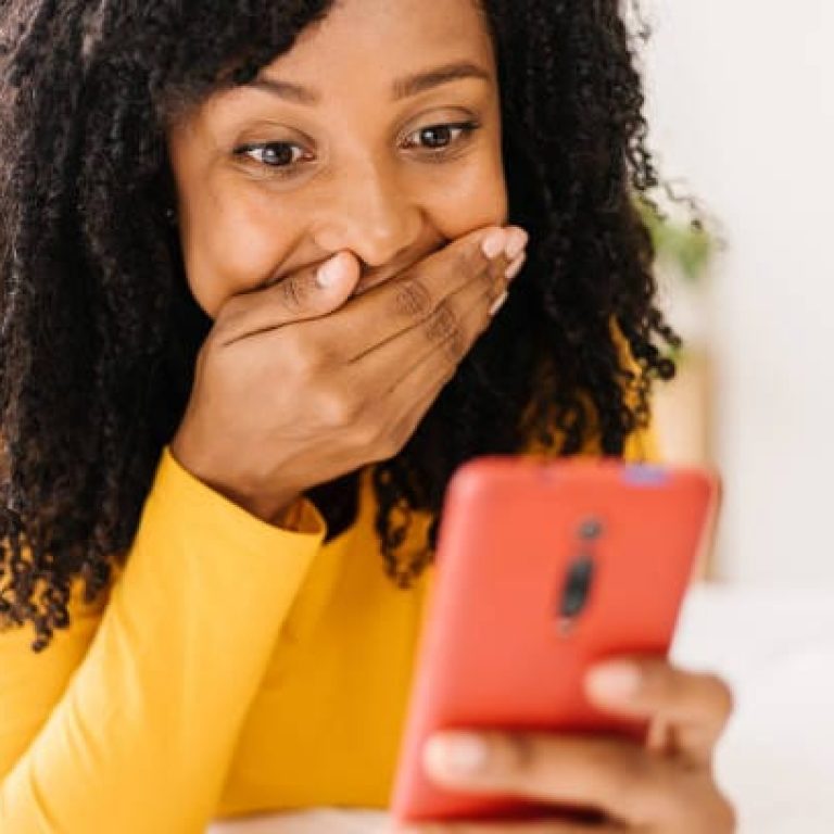 African american woman with a shocked expression on her face while looking at her mobile phone. Technology, social media and emotions concept.