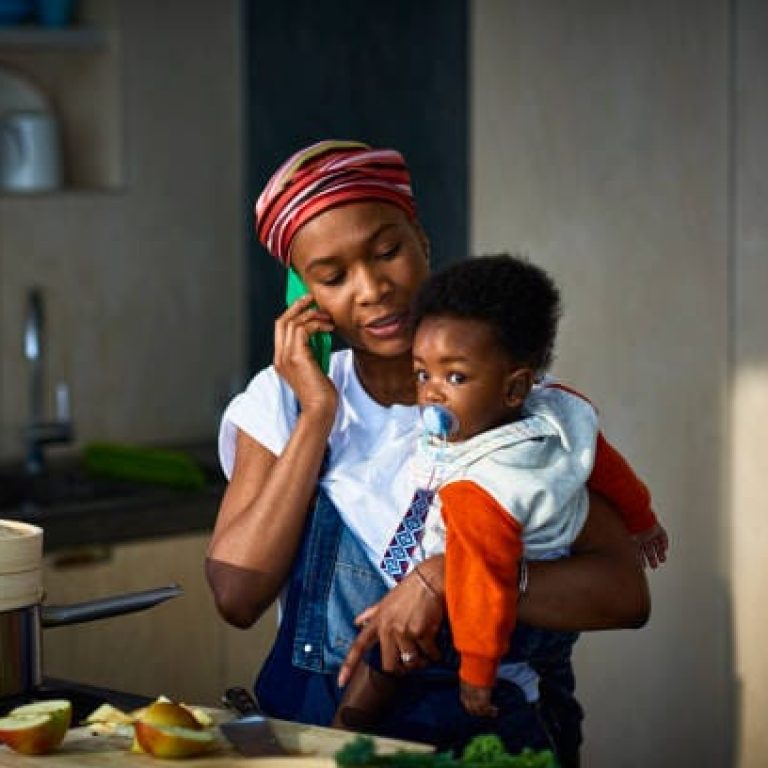 Woman carrying baby son (6-11 months) and talking on mobile phone in kitchen