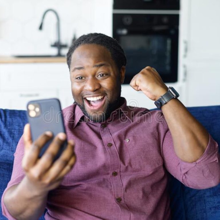hilarious-african-american-man-celebrating-victory-you-lucky-using-smartphone-sitting-sofa-home-winning-online-218089196