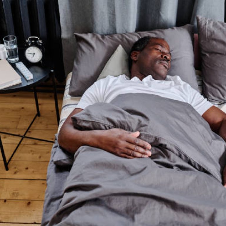 Tired senior man of African ethnicity sleeping under grey blanket with his head on pillow while having rest on comfortable double bed
