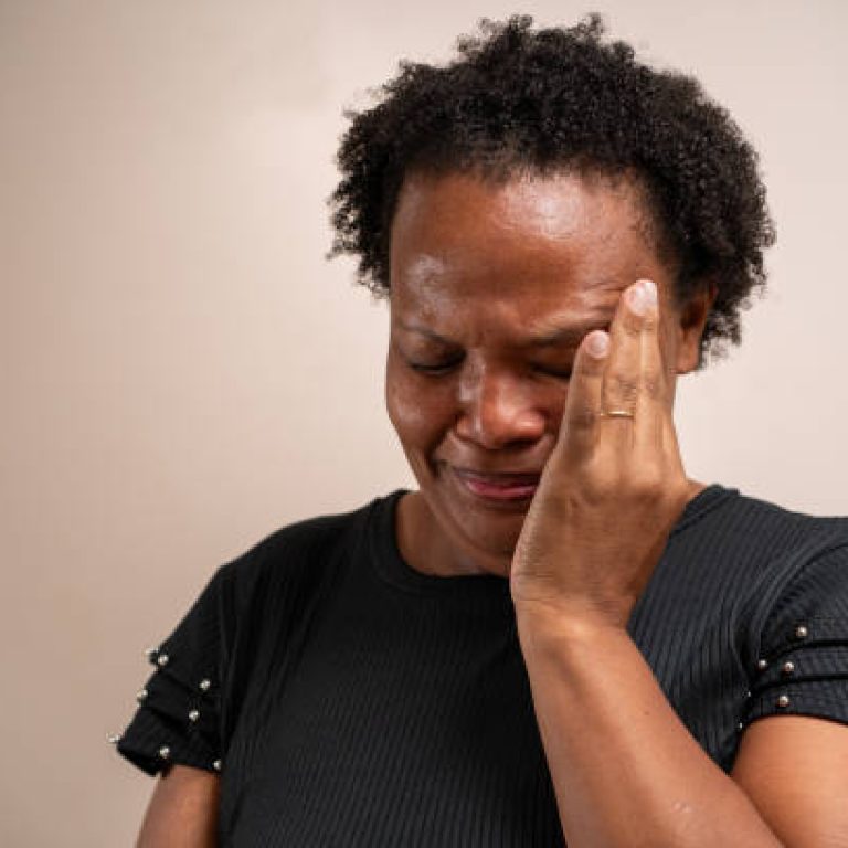 Black woman with hand on face crying on pastel background.