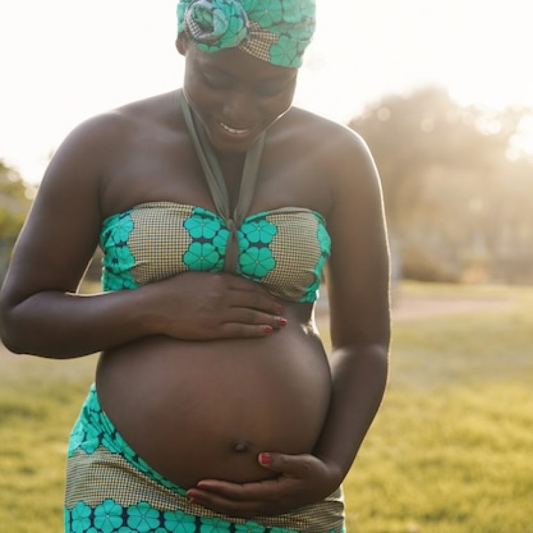young-african-pregnant-woman-having-tender-moment-touching-her-belly-outdoor-city-park-focus-hands-holding_166273-1978